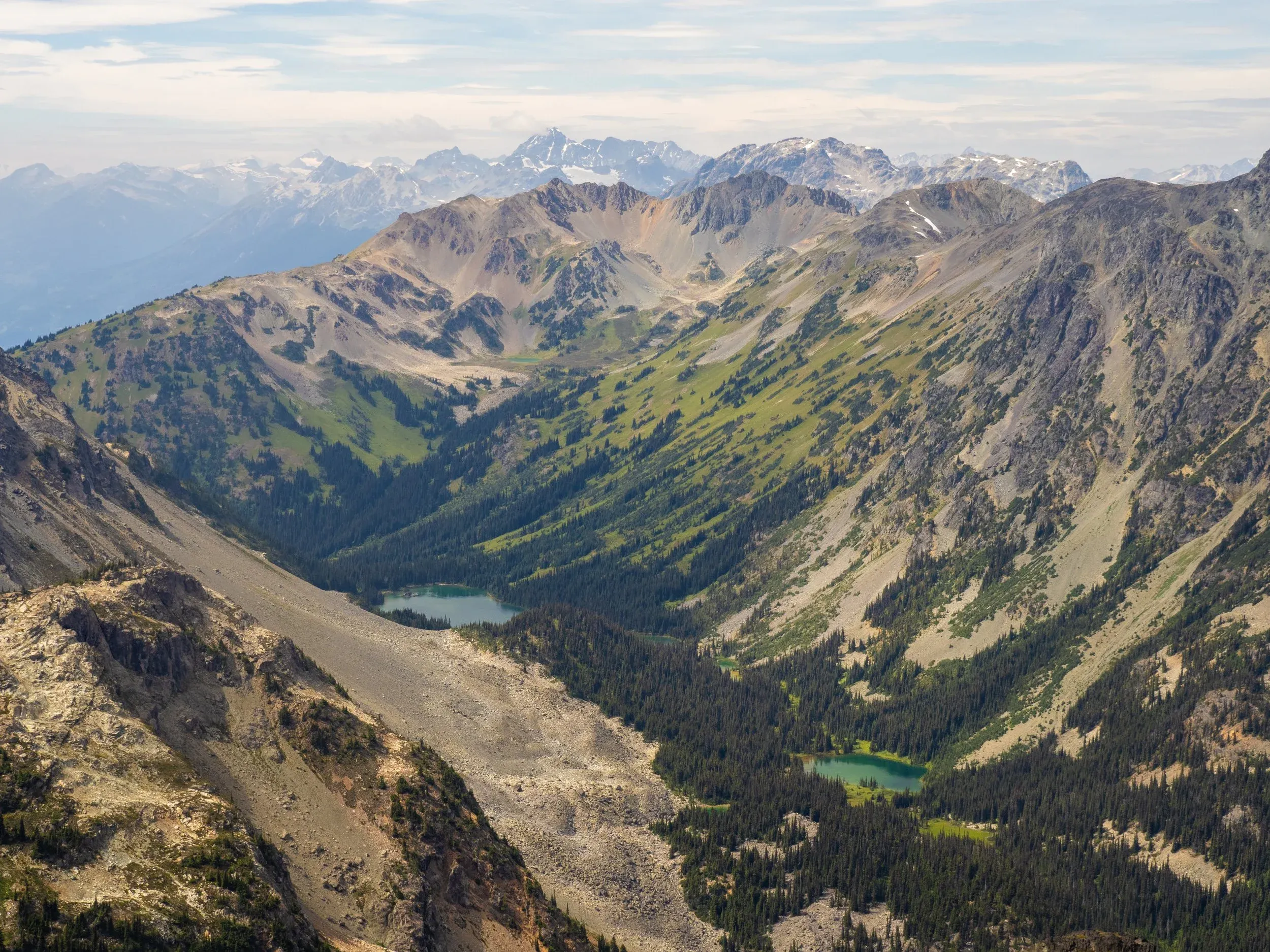 The view west towards the continuation of our route. We would descend down to Ogre Lake at the far end of the valley, then back up verdant slopes with the goal of camping up in the upper basin where another small tarn can be seen. Tenquille Mountain is behind to the right, with Locamotive and Sampson further west.